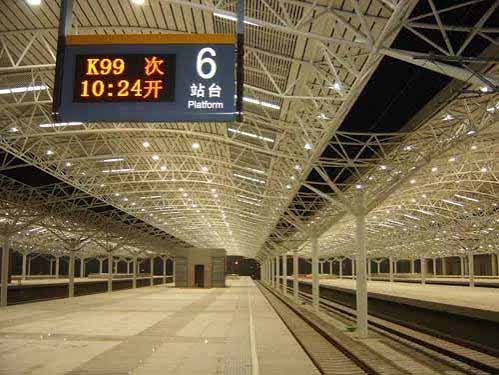 Railway station platform interior with steel roof structure and passenger signage.