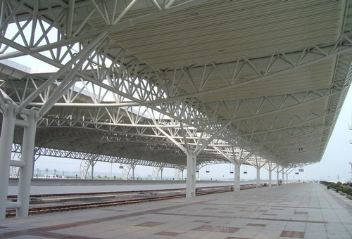 Railway station platform canopy supported by structural steel columns and roof trusses.