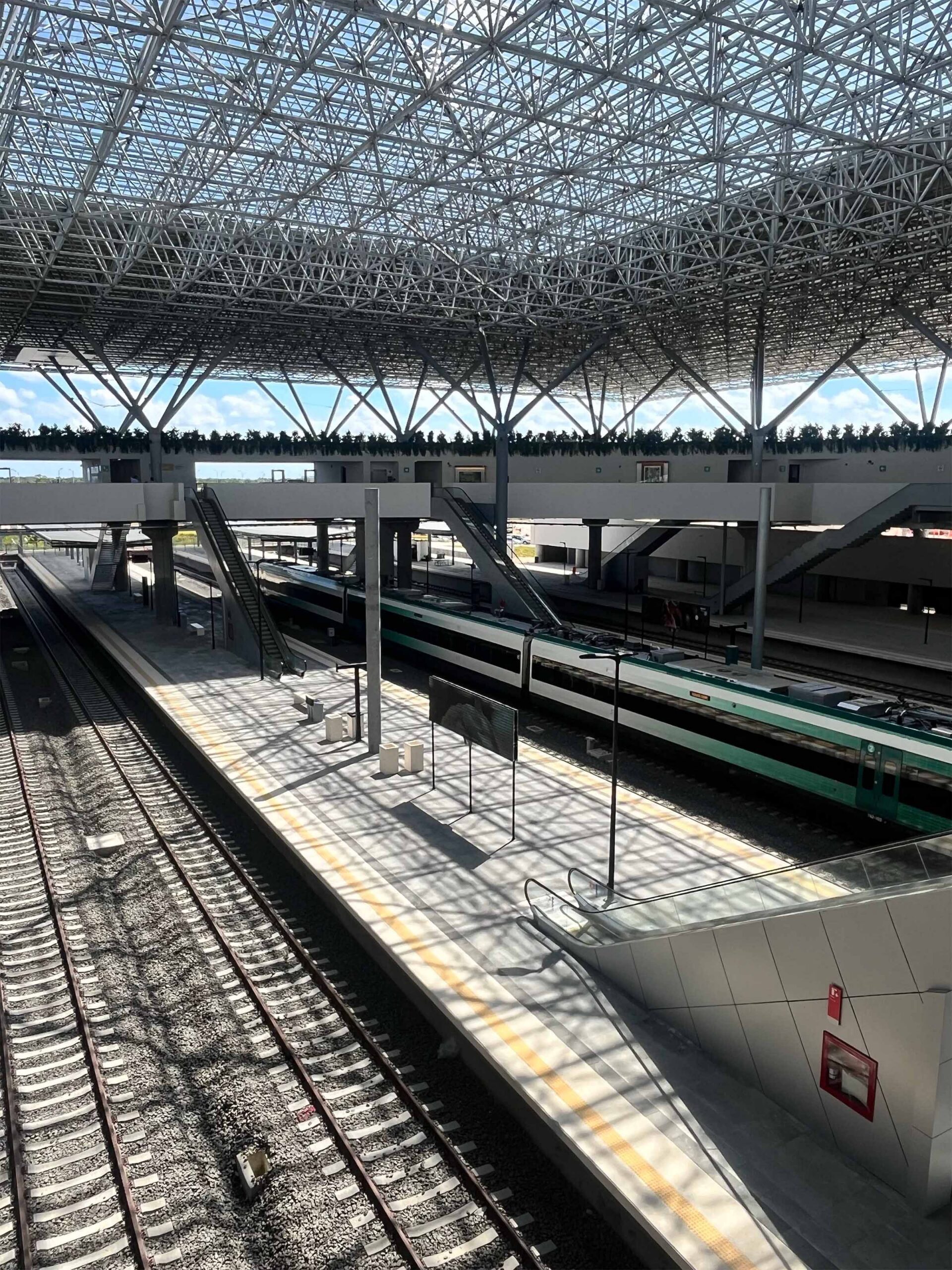 Modern railway station steel structure with platforms, trains and large roof canopy.